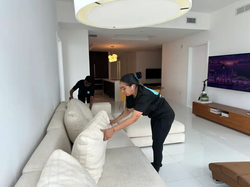 Two professional cleaners putting final touches on a living room sofa during a home cleaning